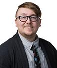 Headshot: Man with glasses in suit smiling at the camera.